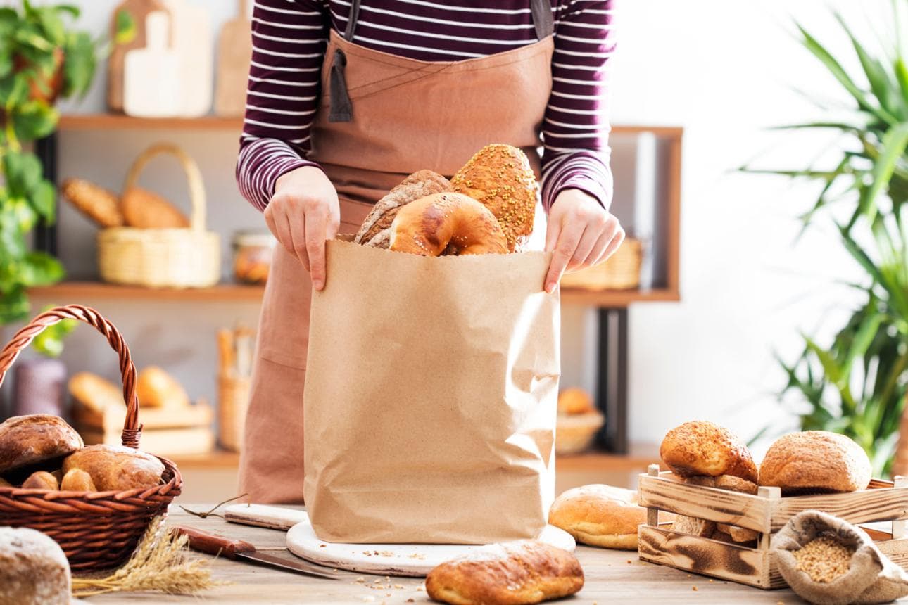 A bakery worker preparing a bag of assorted bread